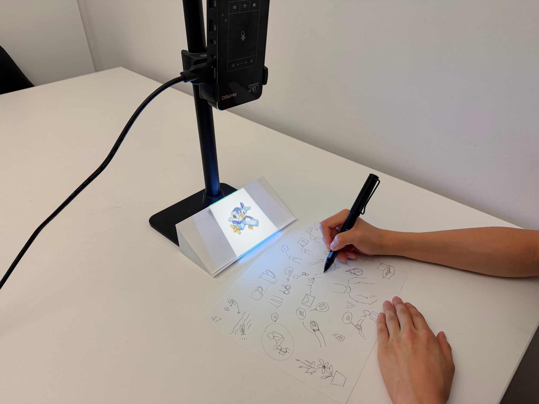 A participant sketching with a smart pen beside a projected AI inspiration image