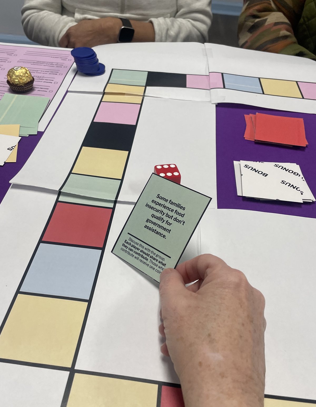 A hand holding a game card over the colorful board